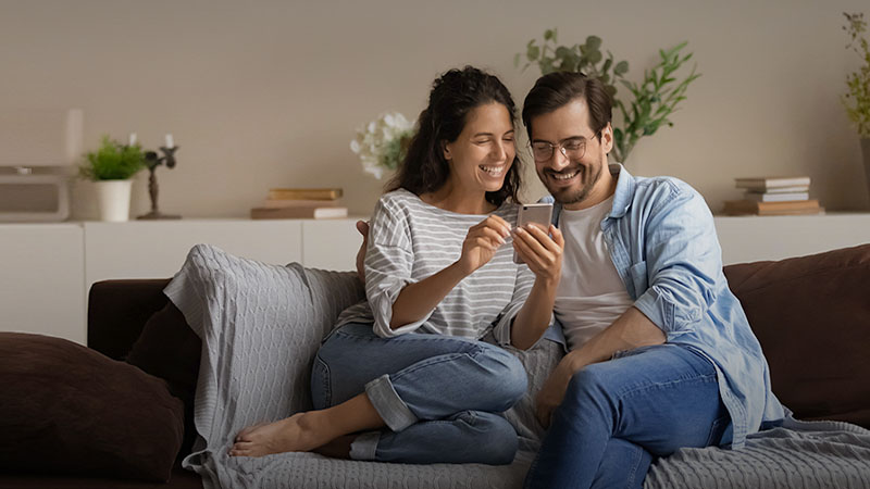 A man and a woman sitting on a sofa and looking into a smartphone