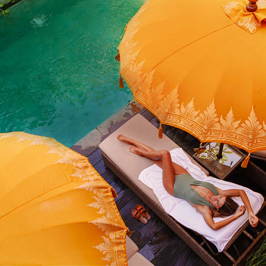 A woman rests on a beach bed under umbrellas