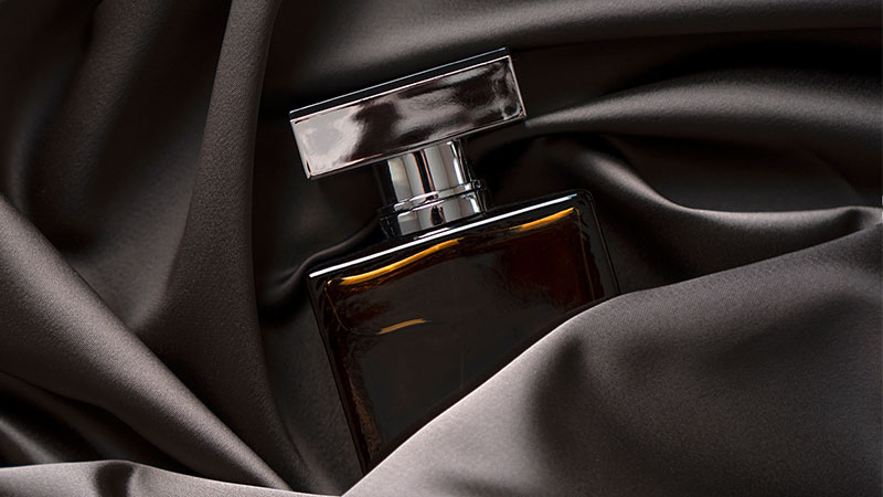 Perfume lies in a dark satin fabric