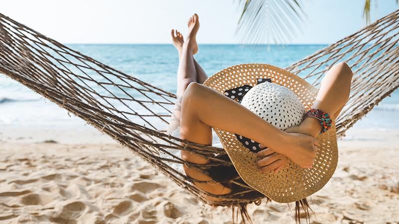 A woman in the big hat lying in the hammock on the beach